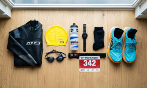 Triathlon gear laid out flat including goggles, wetsuit, and running shoes for a beginner on a budget