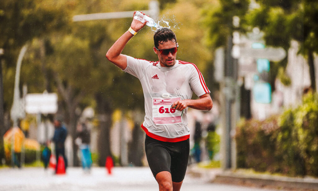 Athlete running in hot sunny conditions pouring water over his head