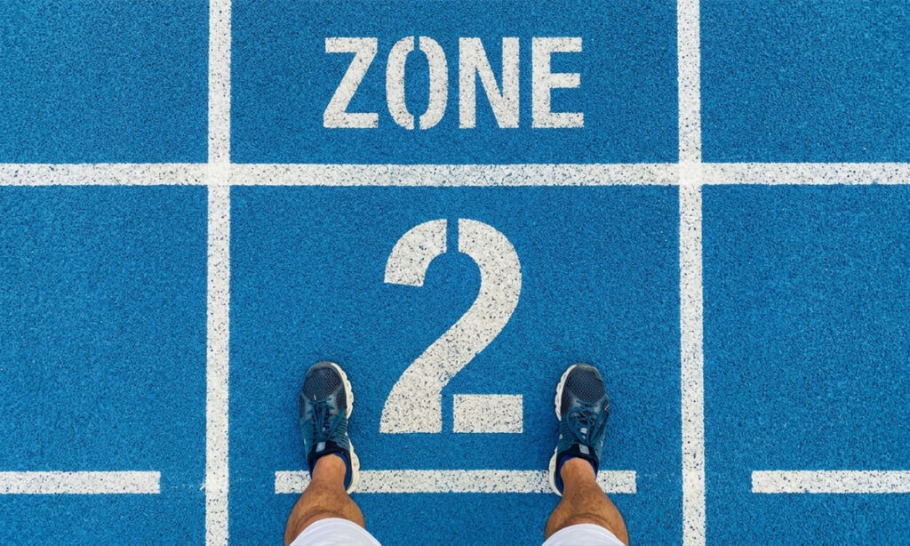 Runner standing on a blue athletics track at the Zone 2 starting line, viewed from above