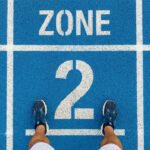 Runner standing on a blue athletics track at the Zone 2 starting line, viewed from above