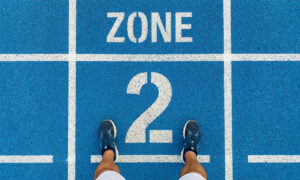 Runner standing on a blue athletics track at the Zone 2 starting line, viewed from above