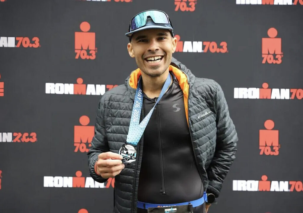 Triathlete holding his Ironman 70.3 Victoria finisher medal in front of the official race backdrop