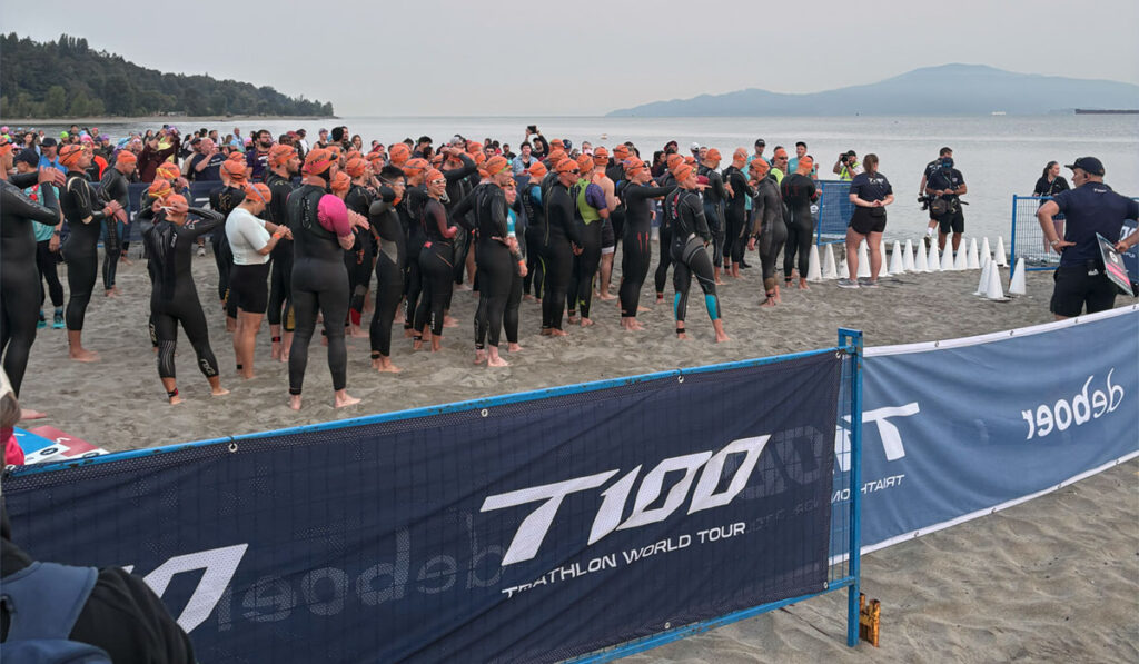 age-group swim wave entering the water at Locarno Beach for the T100 Vancouver Olympic triathlon
